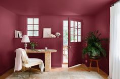 a living room with pink walls and white curtains on the window sill, a chair in front of a table that has a potted plant next to it