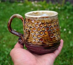 a hand holding a brown and white coffee cup in it's left hand on the grass