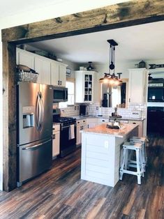 a kitchen with white cabinets and stainless steel appliances, wood flooring and an island in the middle