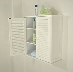 a white cabinet with shutters on the door and shelves above it in a bathroom