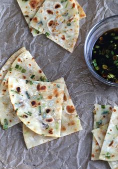 several tortillas on a piece of wax paper next to a bowl of dipping sauce