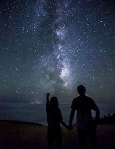 two people standing under the stars in the night sky with their arms outstretched to each other