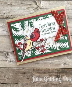 a handmade christmas card with a cardinal and pine tree design on it, sitting on top of a wooden table