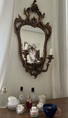 an ornate mirror hangs on the wall above a table with candles and other items in front of it