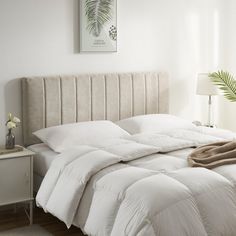 an unmade bed with white comforter and pillows on the headboard in a bedroom