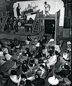 an old black and white photo of people sitting at tables in front of a stage