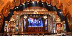 the stage is decorated with gold curtains and drapes for an award ceremony in front of a crowd