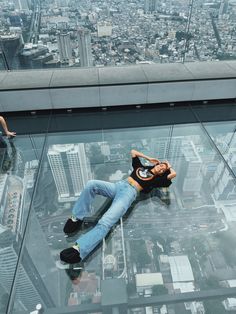 a man laying on top of a glass floor in the middle of a skyscraper building