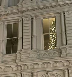 a large white building with a lit christmas tree in the window and clock on it's side