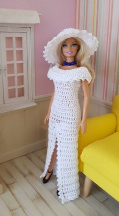 a doll wearing a white crocheted dress and hat in a room with pink walls