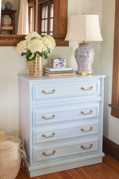 a blue and white chest of drawers with flowers in vases on top next to it