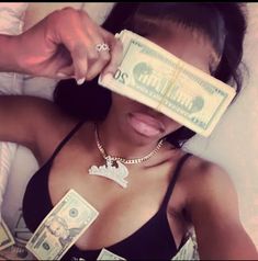 a woman holding money in her hand while laying on top of a bed with white sheets