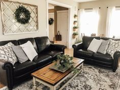 a living room with black leather couches and white pillows on top of a rug