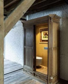 an open door leading to a toilet in a room with exposed ceilings and wood floors