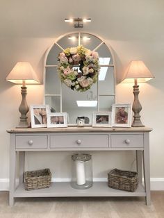 a white console table with flowers and pictures on it in front of a round mirror