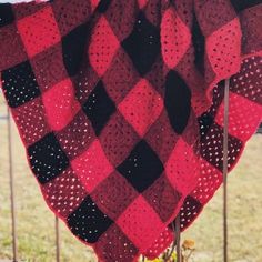 a red and black blanket hanging from a metal pole in front of a fence with grass