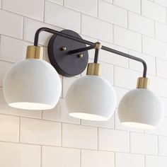 three light fixtures mounted on the wall in a white tiled room with black and gold accents