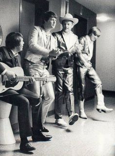 three men in suits and hats are playing the guitar while another man sits on a toilet