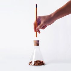 a hand holding a pencil over a small glass bottle filled with chocolate chips and cinnamons