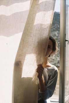 a woman is holding up the curtains in front of her