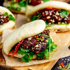 small sandwiches with meat, lettuce and sauces on wooden cutting board next to utensils