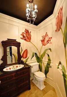 a bathroom decorated with pink flowers and green leaves on the wall, along with a white toilet