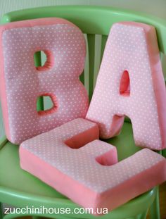 the letters are pink and white with polka dots on them, sitting on a green chair