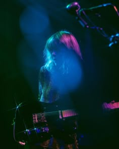 a woman with long hair playing a keyboard in front of a microphone and some lights