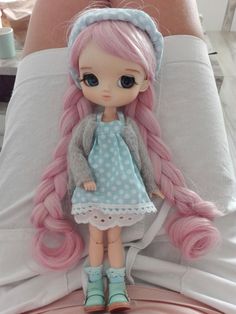 a doll with pink hair is sitting on a bed