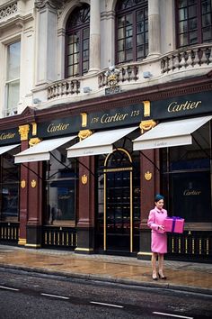 a woman in a pink dress is standing on the side of the street holding a box