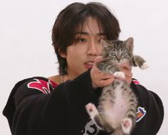 a young man holding a kitten in his right hand and looking at the camera while wearing a black sweater