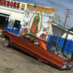 an old red car parked in front of a building with a mural on it's side