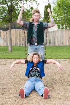 a man and woman sitting on swings in the park, one holding onto the other's back