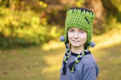 a young boy wearing a green crocheted hat with ear flaps and braids