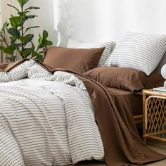 a bed covered in brown and white striped comforter next to a plant on a side table