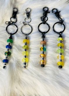 four different colored beads are hanging from key chains on a white furnishing area