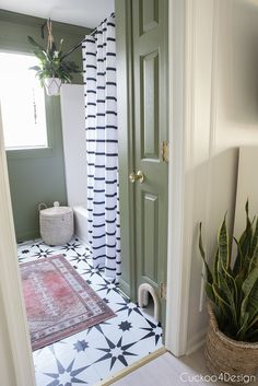 a bathroom with a green door and black and white tile on the floor next to a potted plant