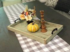 a wooden tray with flowers and candles on it sitting on a checkered table cloth