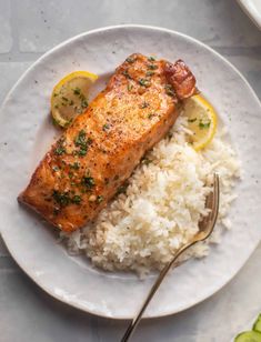 a white plate topped with rice and salmon next to a fork on a tablecloth