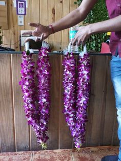 two purple flowers are hanging from the side of a wooden wall and being held by a person