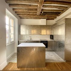 an empty kitchen with stainless steel appliances and wood beams on the ceiling, along with hardwood flooring