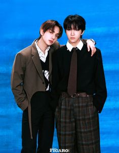 two young men standing next to each other in front of a blue background wearing suits and ties