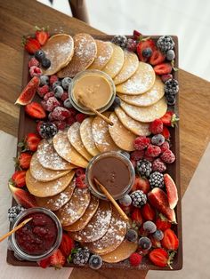 a platter filled with pancakes and fruit on top of a wooden table next to dipping sauce