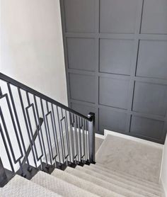 a stair case with black railing and white carpet on the bottom handrail, next to a gray paneled wall