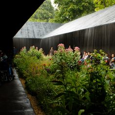 many people are sitting in chairs near the water wall and flowers on the side of the building