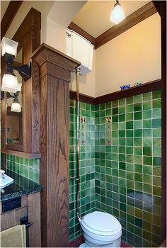 a bathroom with green tile and wood accents on the walls, along with a white toilet