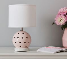 a pink vase with hearts on it sitting next to a lamp and a book,