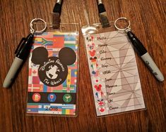 two mickey mouse luggage tags on top of a wooden table next to markers and pens