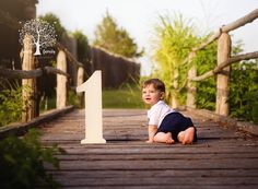 a baby boy sitting on the ground in front of a number one sign for his first birthday