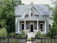 a small house with a porch and two windows on the front, surrounded by greenery